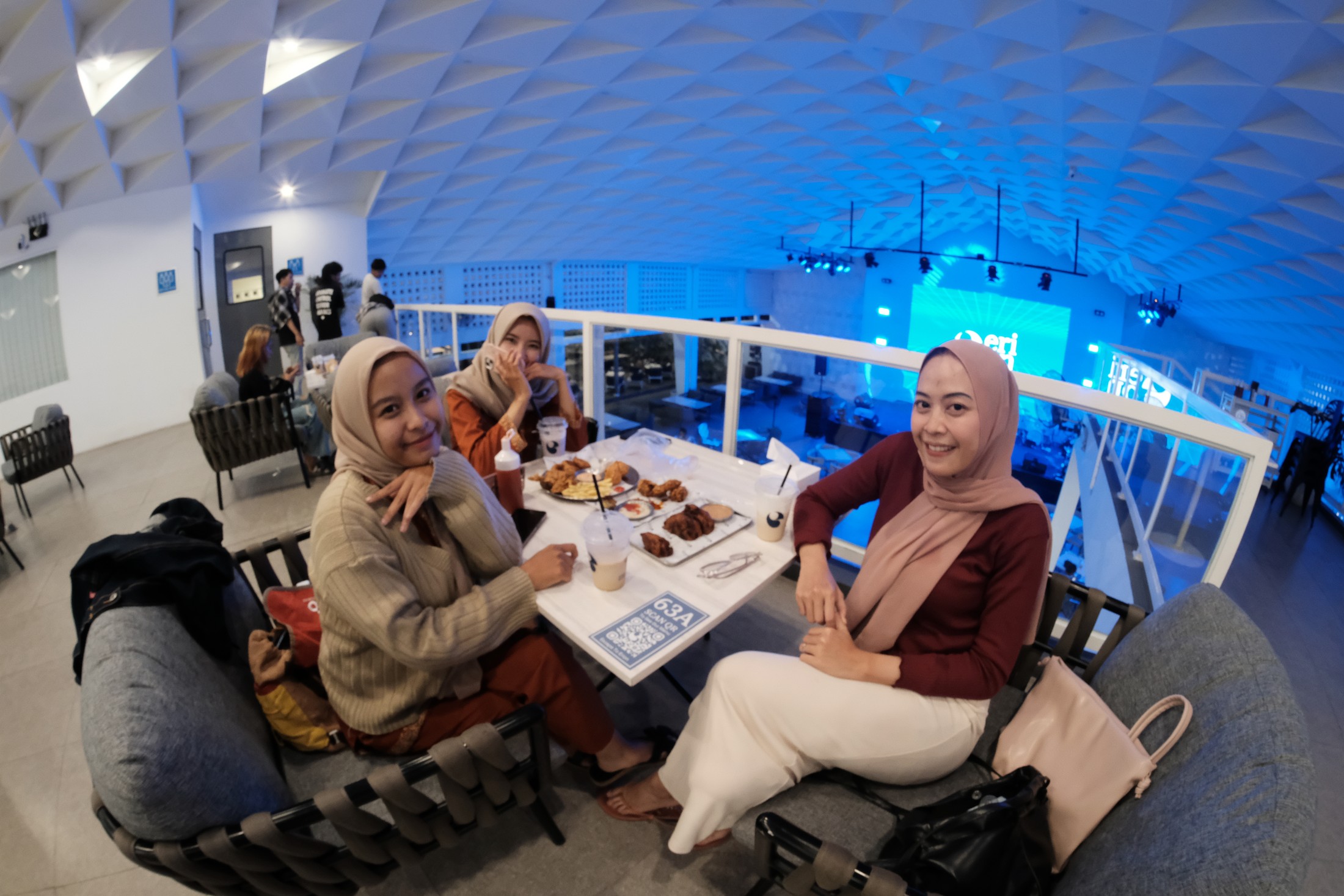 Tiga teman duduk dengan kopi dan makanan di dekat panggung Chillscape.